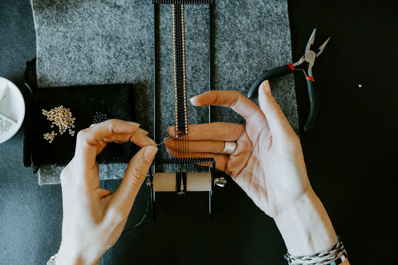 Mains de créatrice de bijoux assemblant un bracelet en perles avec ses outils sur l'établi