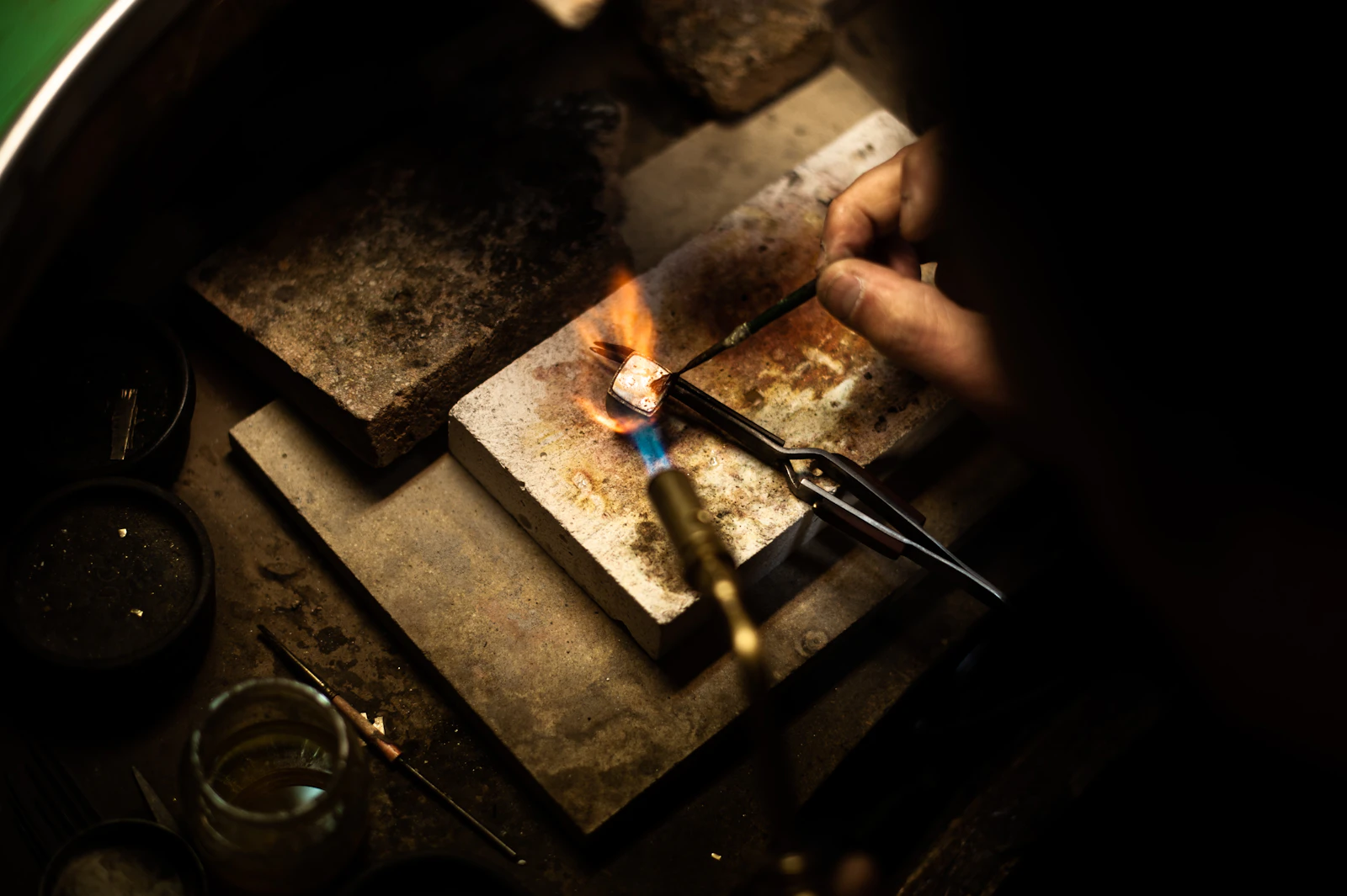 Mains d'artisane bijoutière au travail dans son atelier, ciseaux et outils sur l'établi