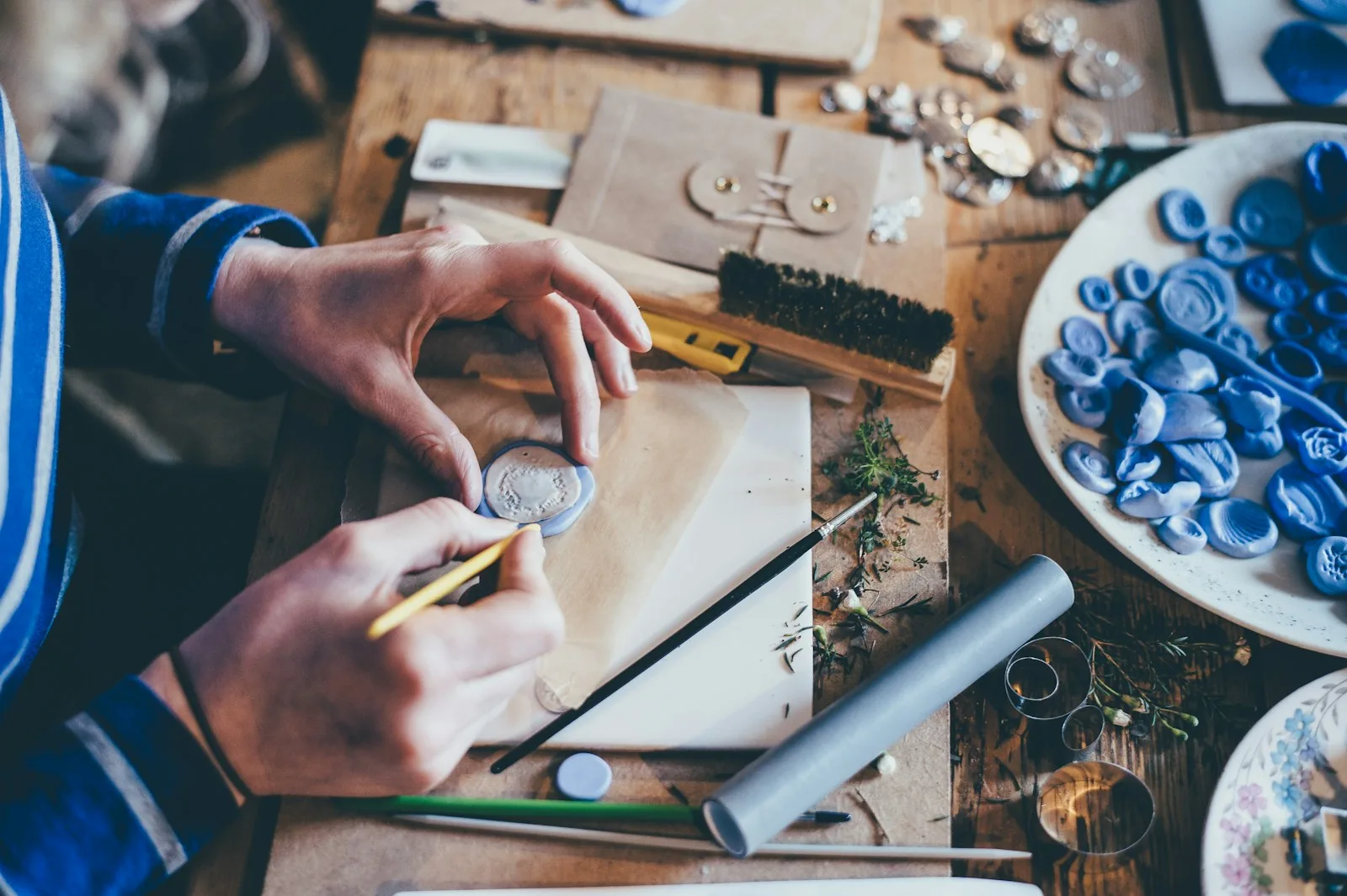 Mains d'artisane au travail sur un atelier rempli de matières premières et de petits objets créatifs